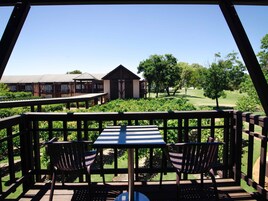 Uma área de estar coberta ao ar livre, com mesa e cadeiras, com vista para um edifício e um campo de golfe.