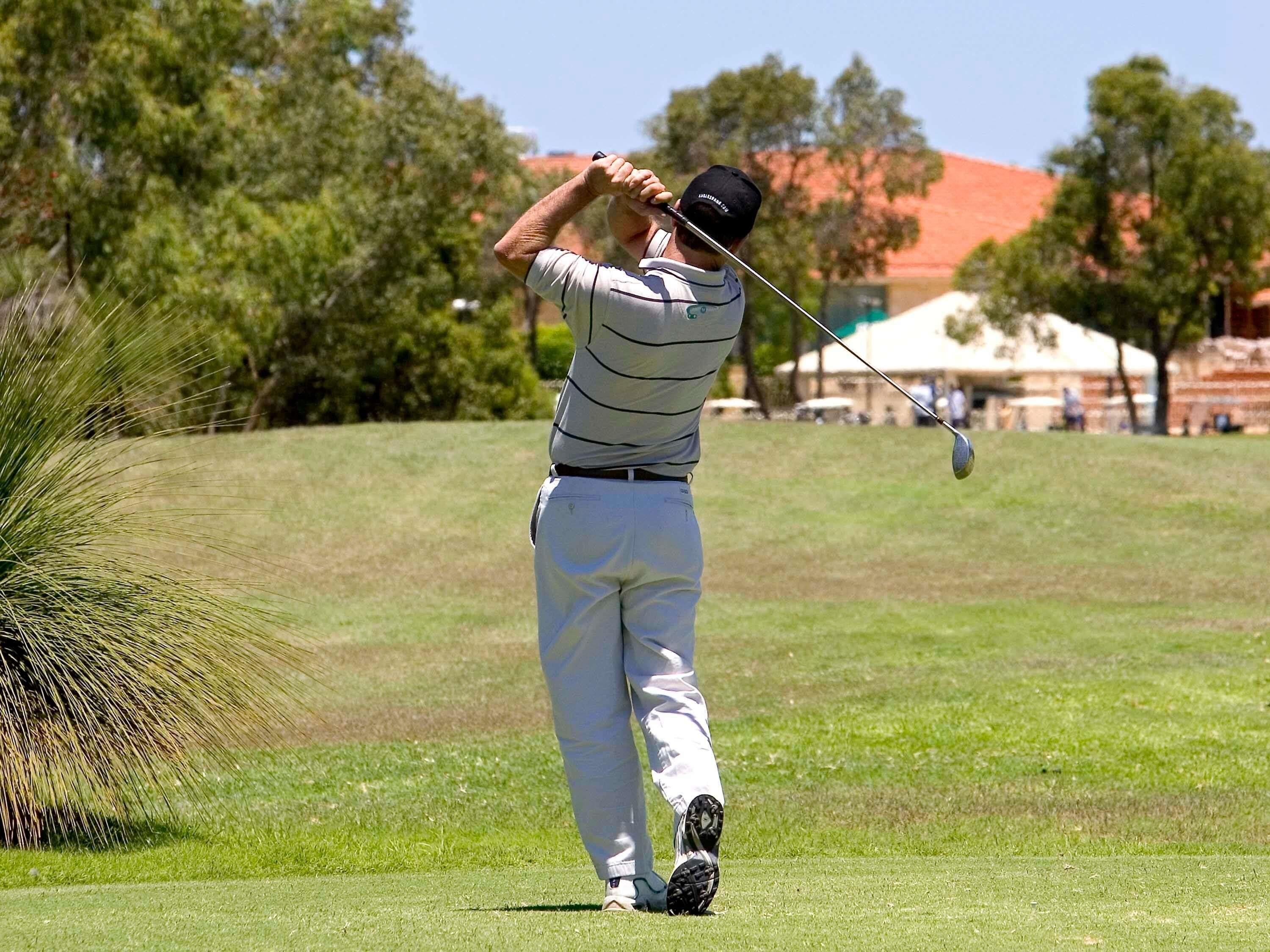 A person playing golf on a well-maintained course with trees and a building in the background.