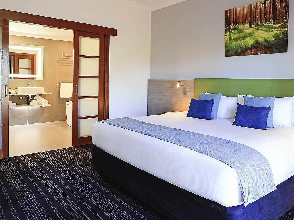A hotel room with a large bed, a bathroom with a mirror, and a painting on the wall.