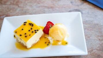 Prato de sobremesa com uma fatia de cheesecake e uma bola de sorvete de baunilha, decorado com morango e sementes.