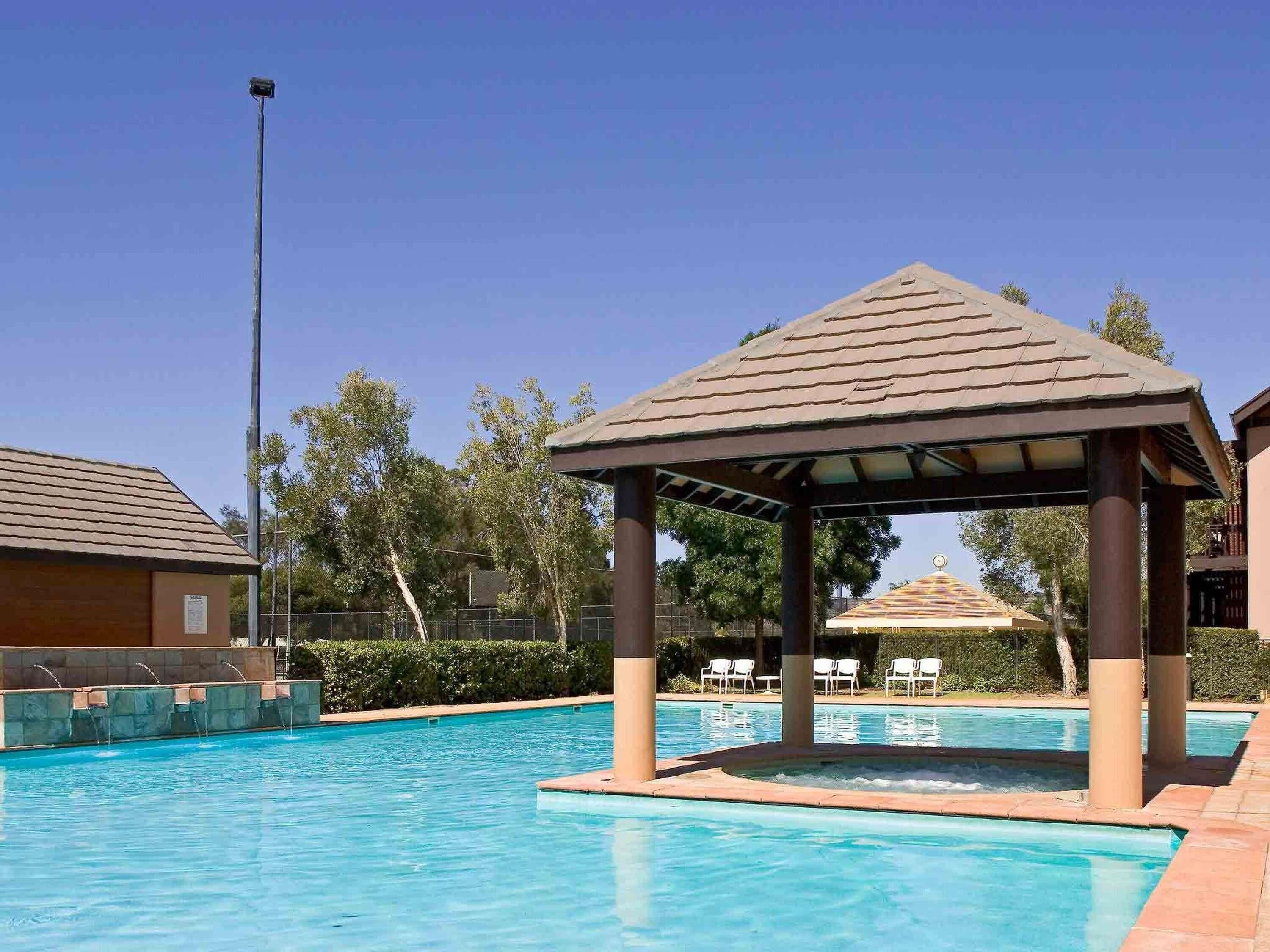 Une piscine avec un kiosque, des chaises longues et un ciel dégagé.