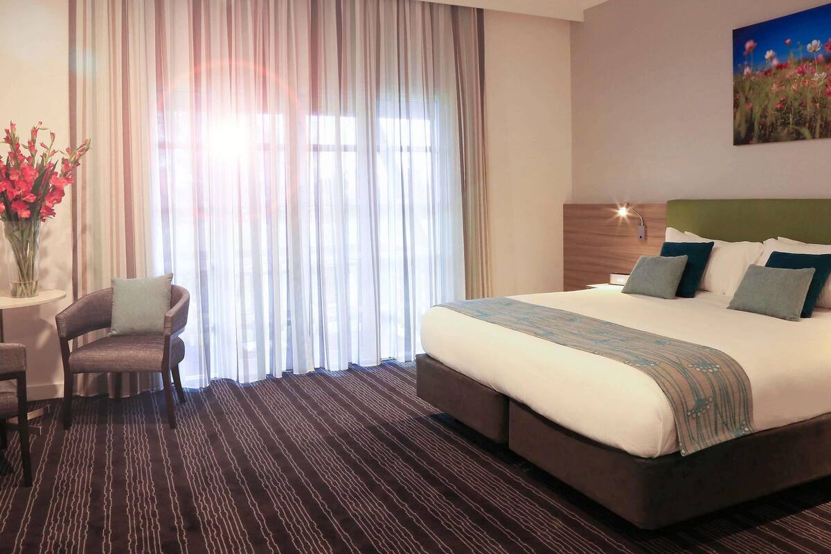 A hotel room with a large bed, a chair, a desk, and a painting on the wall.
