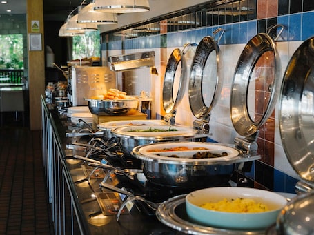 A buffet setup with various dishes in metal serving containers, a tiled backsplash, and overhead lighting.. Novotel Vines Resort Swan Valley