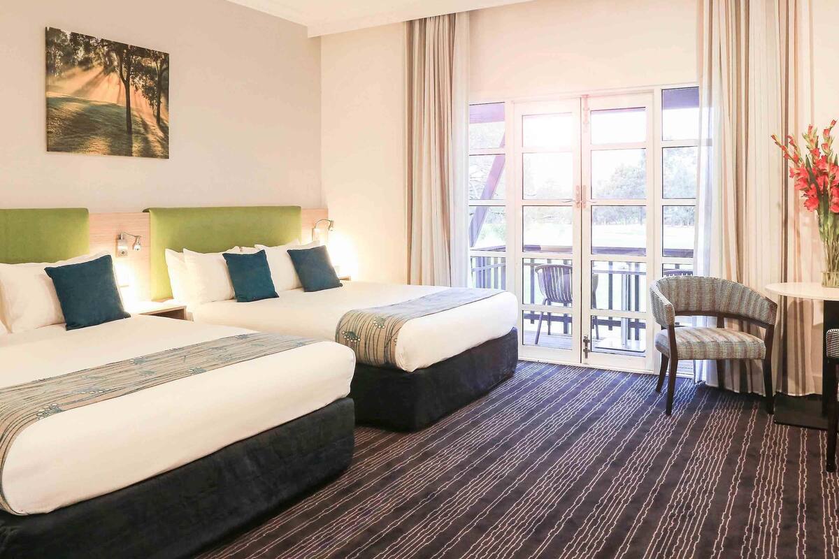 A hotel room with two beds, a balcony with a chair, and a painting on the wall.