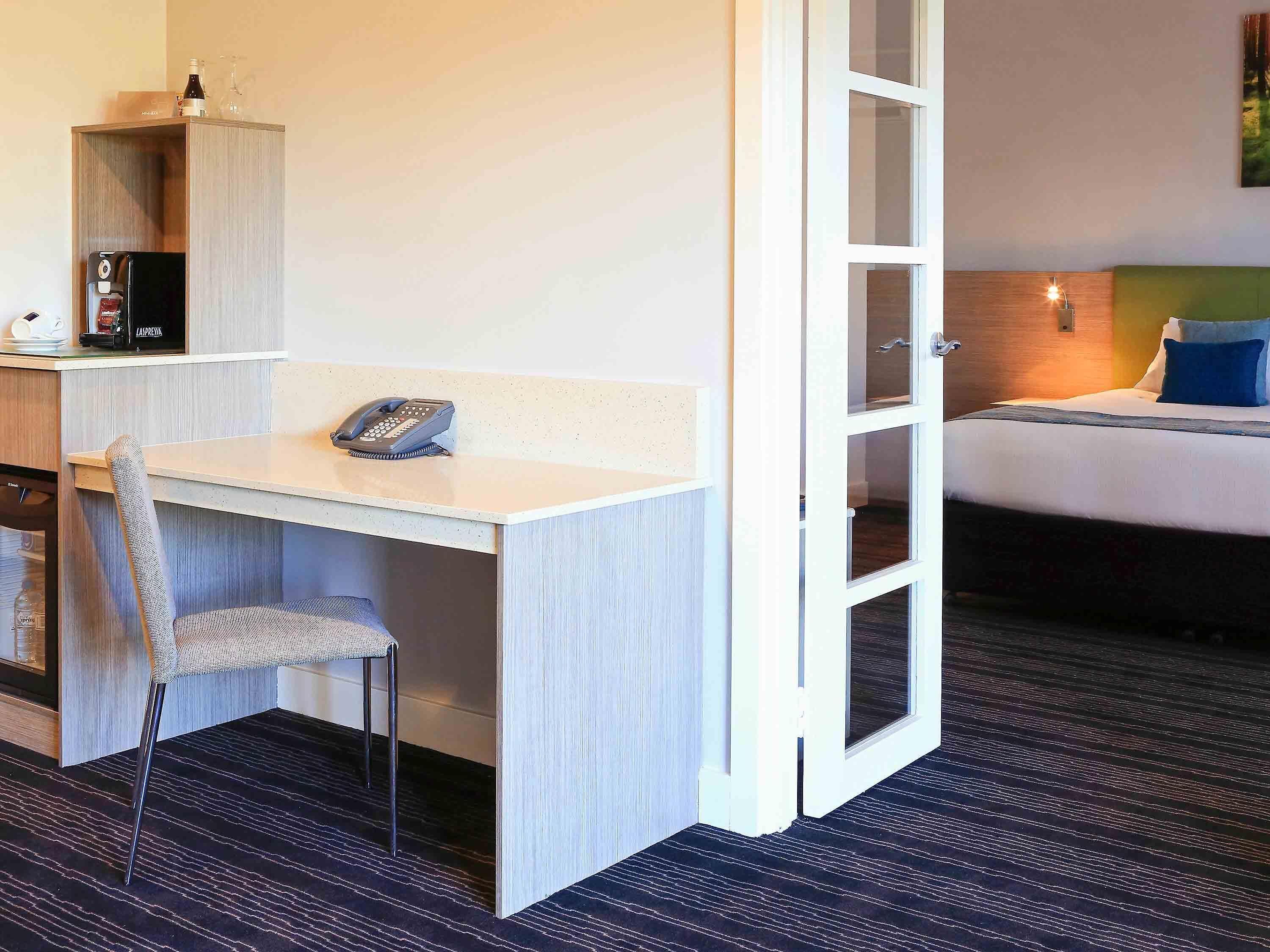 Et hotelværelse med skrivebord, stol, minibar og en seng med sengegavl.