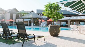 A poolside area with lounge chairs, a large planter with a tree, and umbrellas. - Novotel Vines Resort Swan Valley (The Vines)