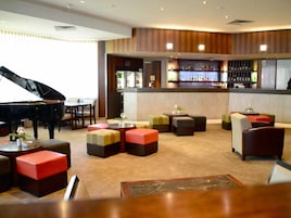 Un vestíbulo de hotel con un piano de cola, una zona de bar y arreglos de asientos.
