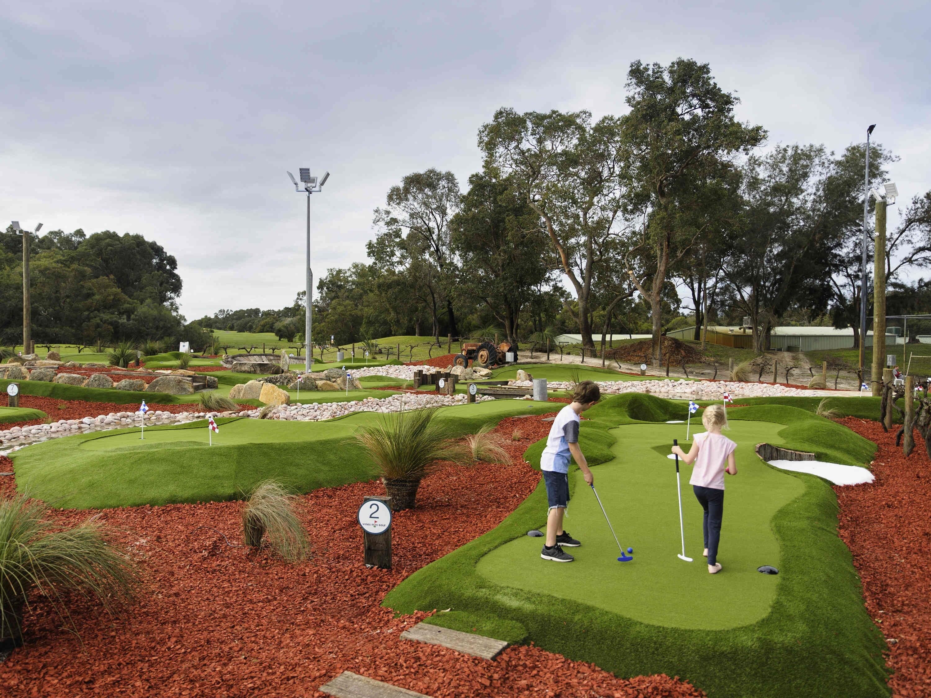 A miniature golf course with a well-maintained green fairway, a putting green, and a flagstick.