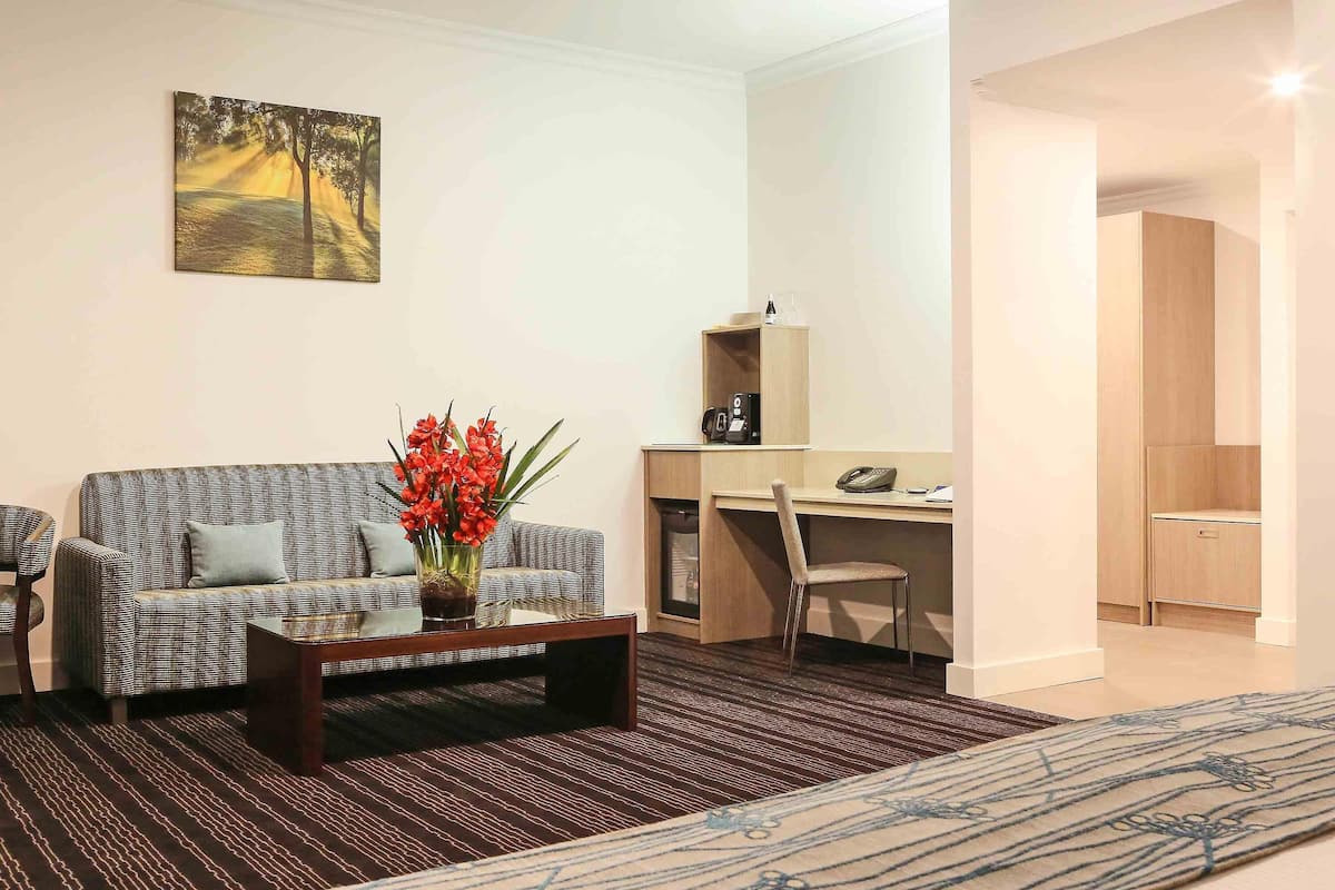 Un salon moderne comprenant un canapé, une table basse ornée d’un vase de fleurs, un bureau avec une chaise et un lit recouvert d’une couvre-lit à motifs.