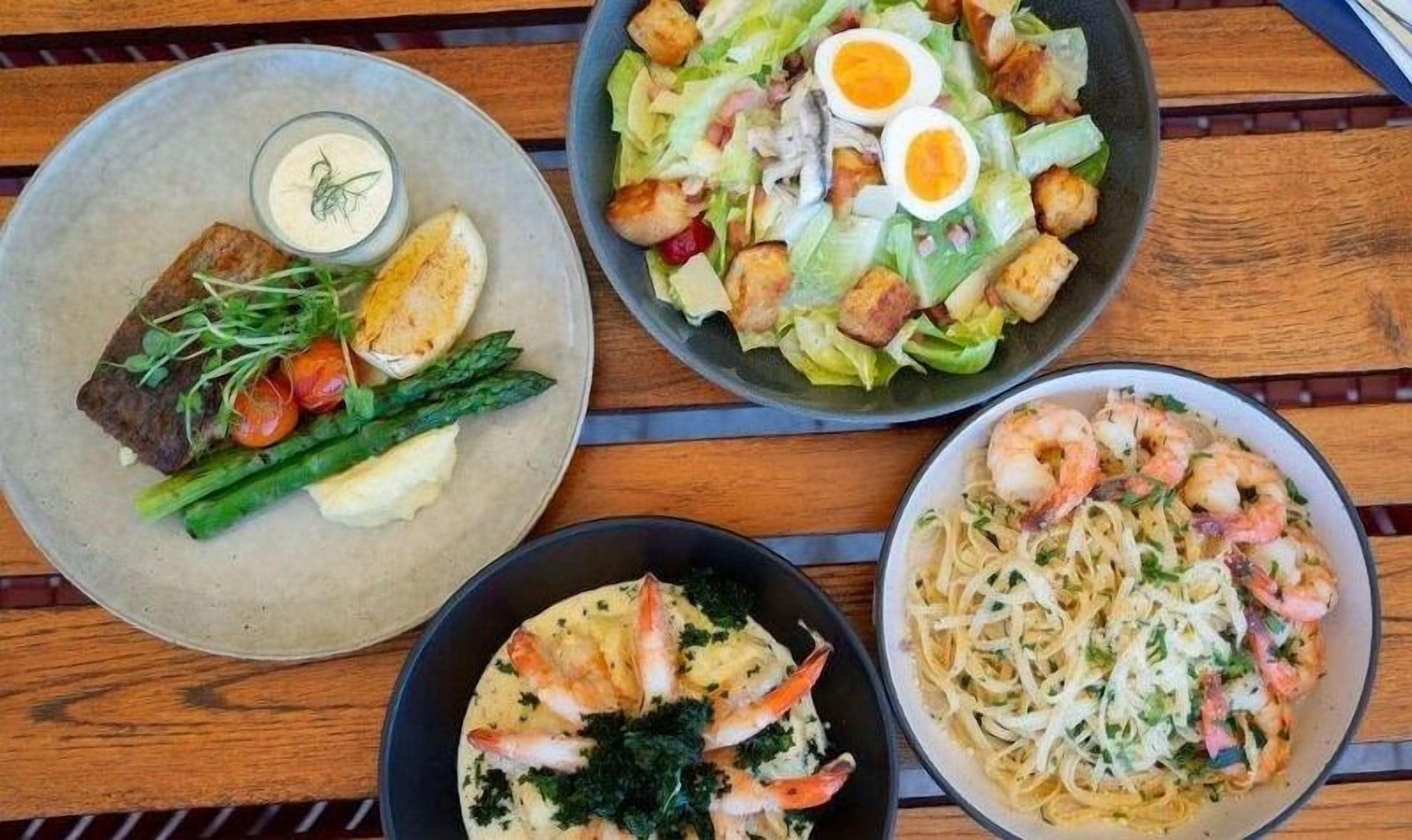 Tres platos: una ensalada con huevos y tostadas, pasta con mariscos y un plato de carne, espárragos y salsa.