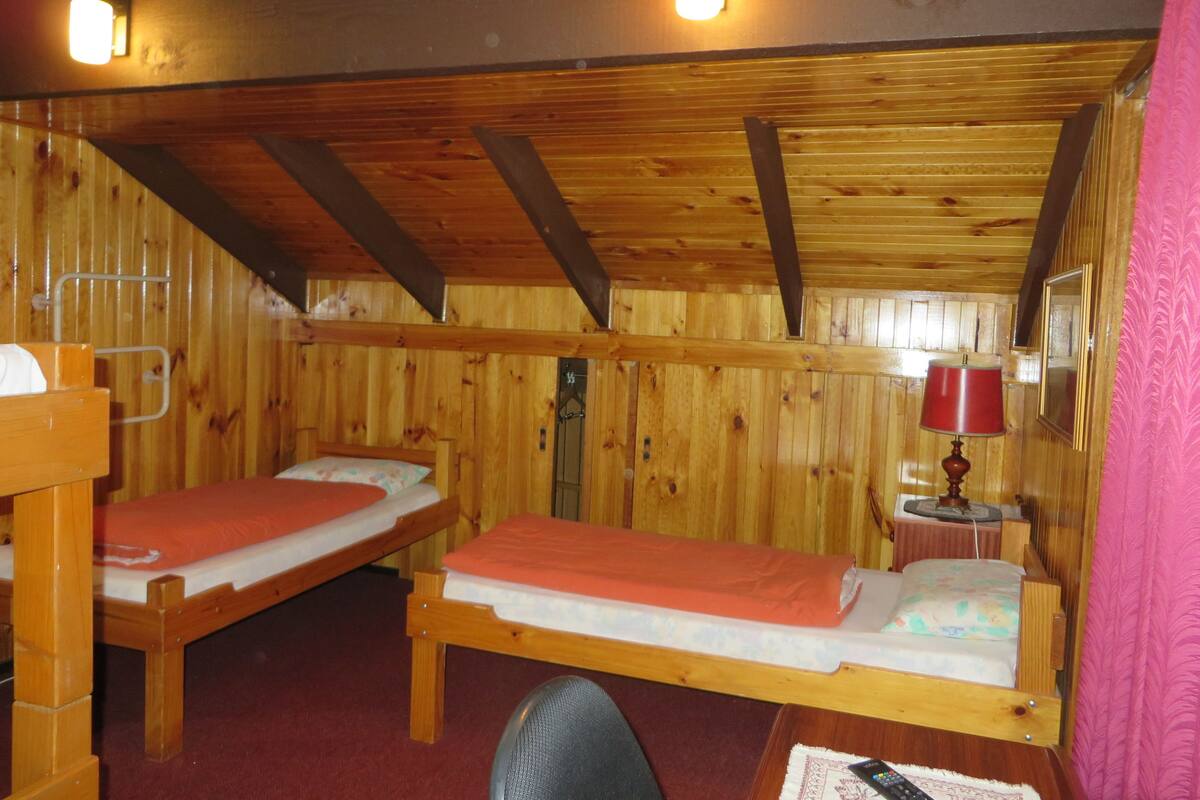 A cabin with two wooden bunk beds, a small table with a lamp, and a wooden ceiling with exposed beams.
