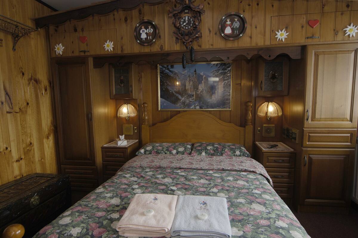 A wooden room with a bed, nightstands, and a wall clock.