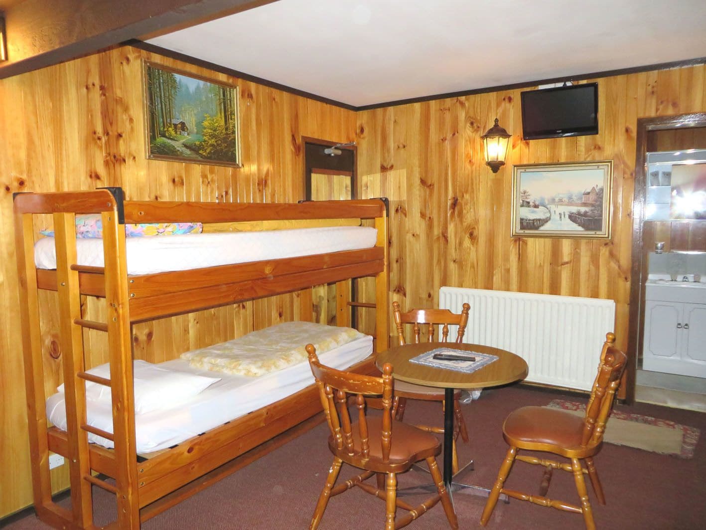 A bunk bed with a table and chairs in a room with wooden walls and a painting.