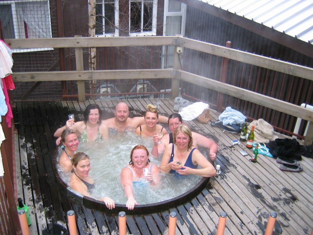 A group of people in a wooden hot tub surrounded by a wooden deck.