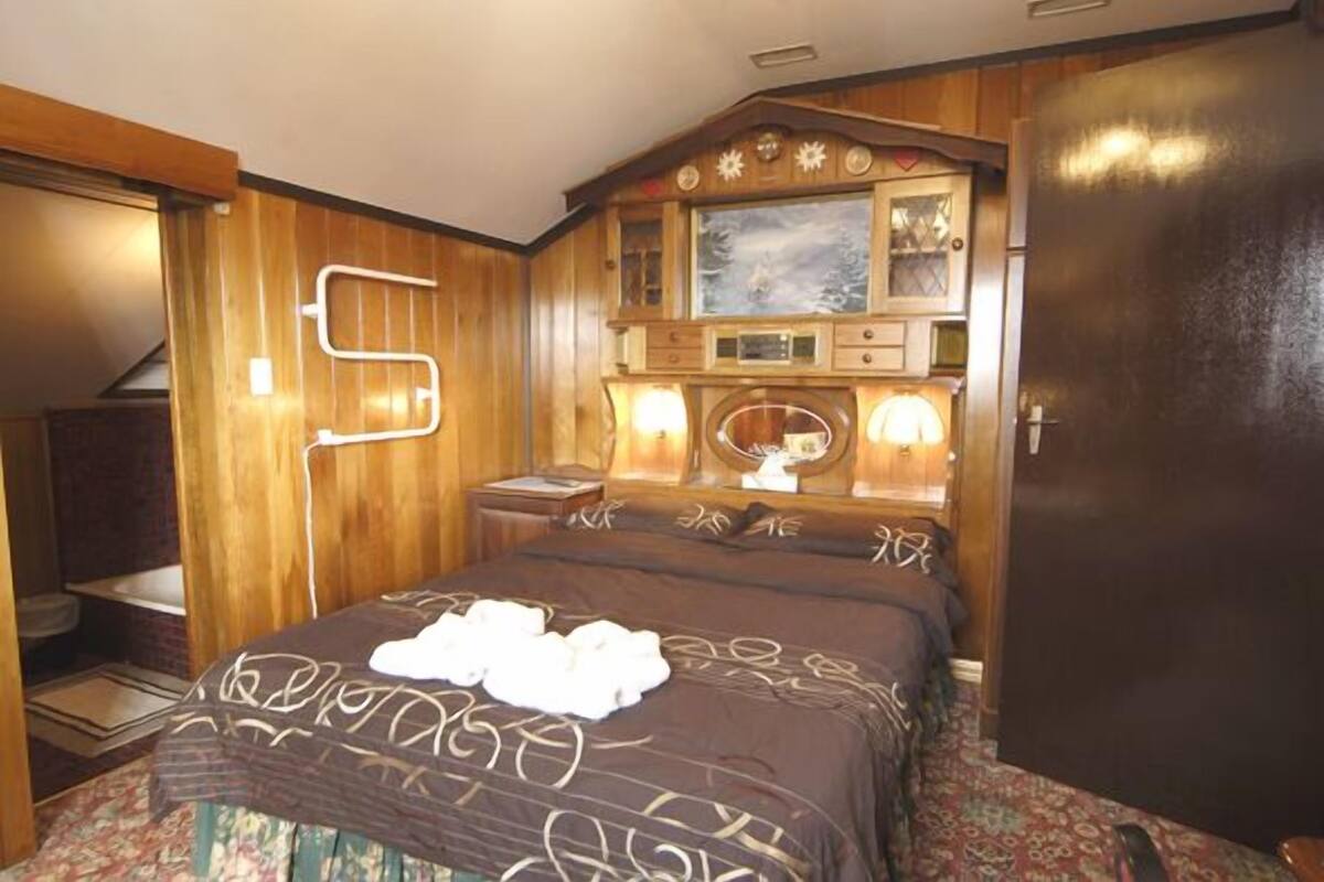 A wooden-paneled bedroom with a bed, a dresser, and a mirror.