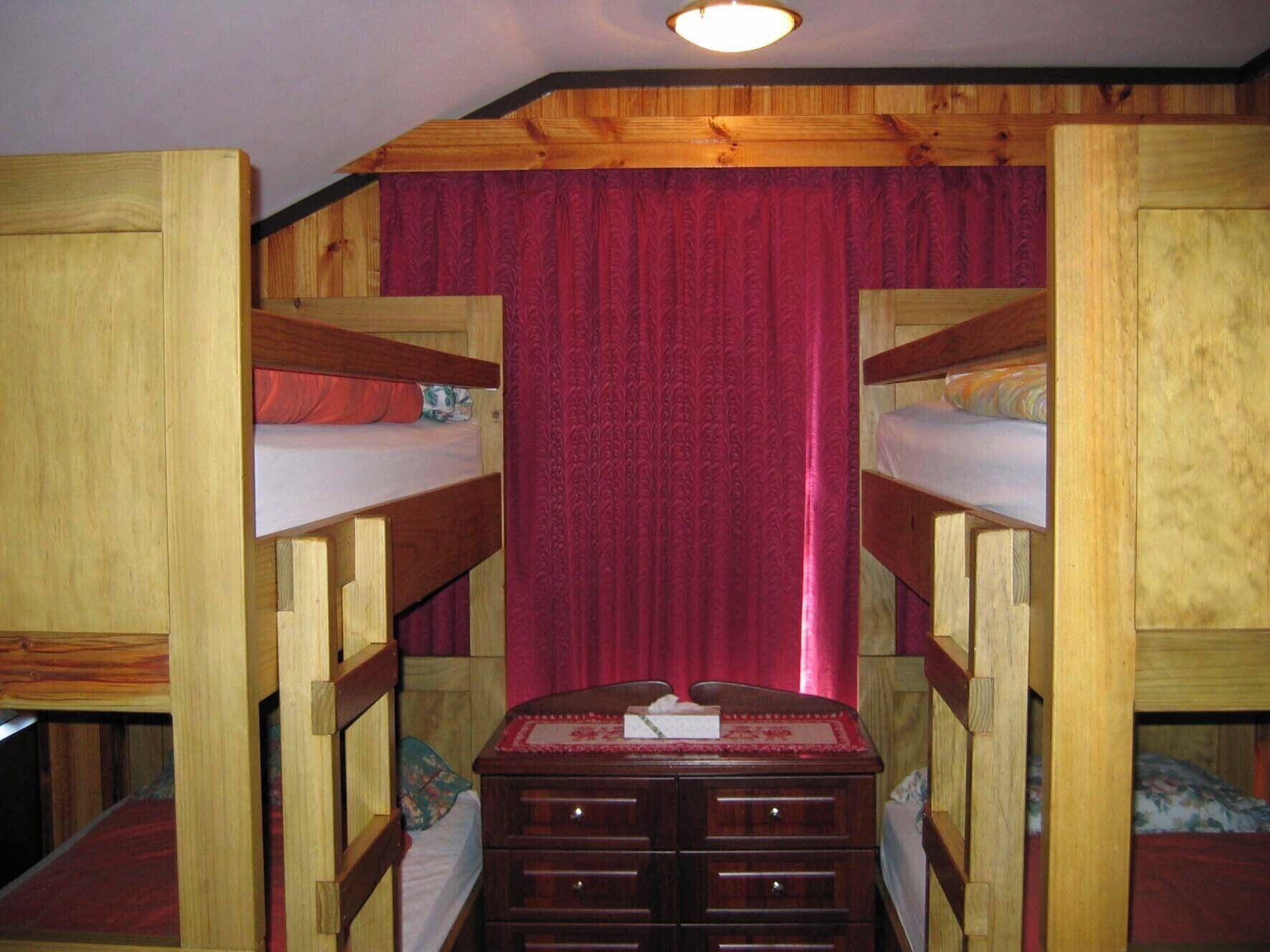 A room with two bunk beds, a wooden dresser, and a red curtain.