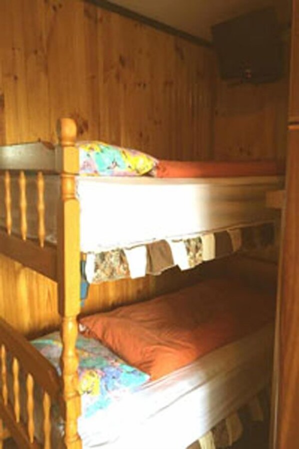Una cama litera con cabecera de madera y una cama inferior con una manta colorida.