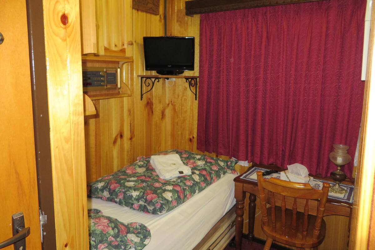 A wooden room with a bed, a television mounted on the wall, and a desk with a chair.