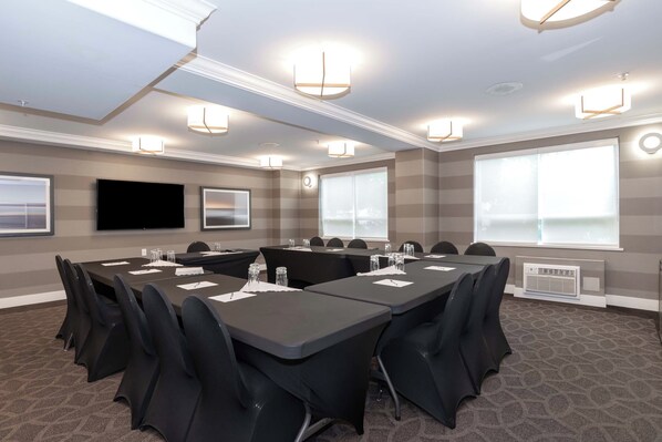 Un salón de conferencias con una larga mesa, sillas negras y luces en el techo.