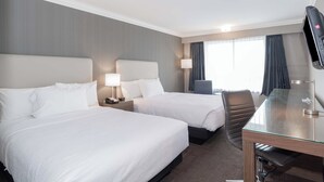 Une chambre d’hôtel avec deux lits, un bureau, une chaise, une télévision et une fenêtre avec des rideaux.