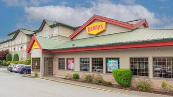 Ein Denny's Restaurant mit grüner Dachbegrünung und beige farbenen Außenwänden, gelegen auf einem Parkplatz mit mehreren Autos.