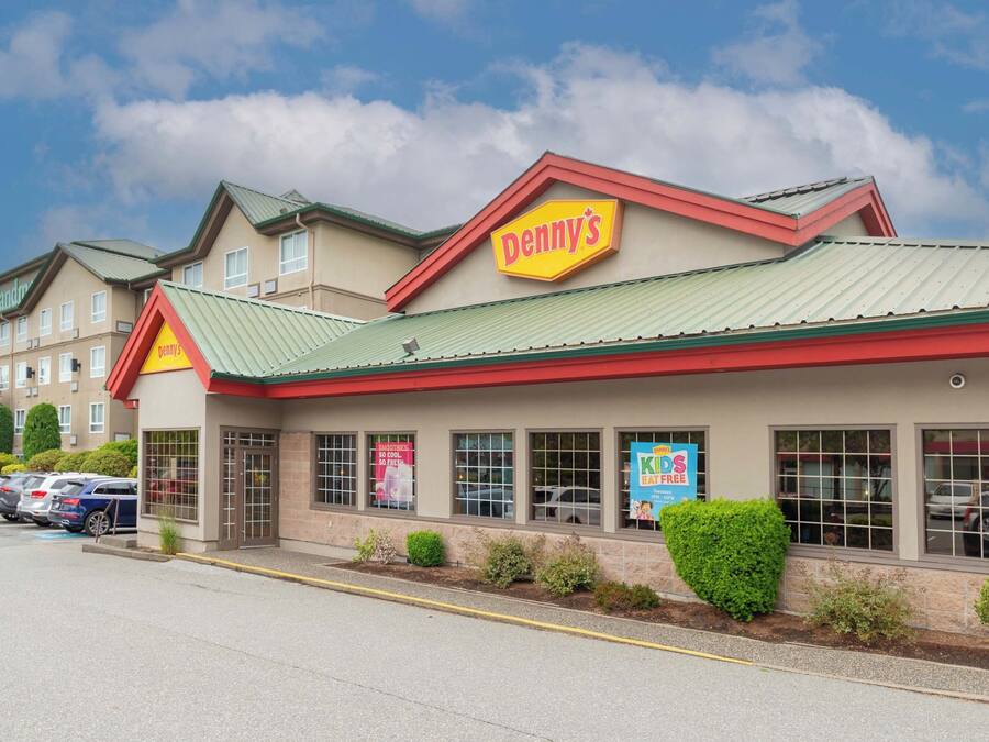 Ein Denny's Restaurant mit grüner Dachbegrünung und beige farbenen Außenwänden, gelegen auf einem Parkplatz mit mehreren Autos.