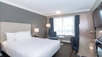 A hotel room with a large bed, a desk with a TV, a chair, and a small table.