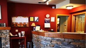 A reception area with a stone wall, a wooden reception desk, a clock, framed pictures, and a bulletin board with notices. - Canadian Rockies Chalets by Trilink (Canmore)