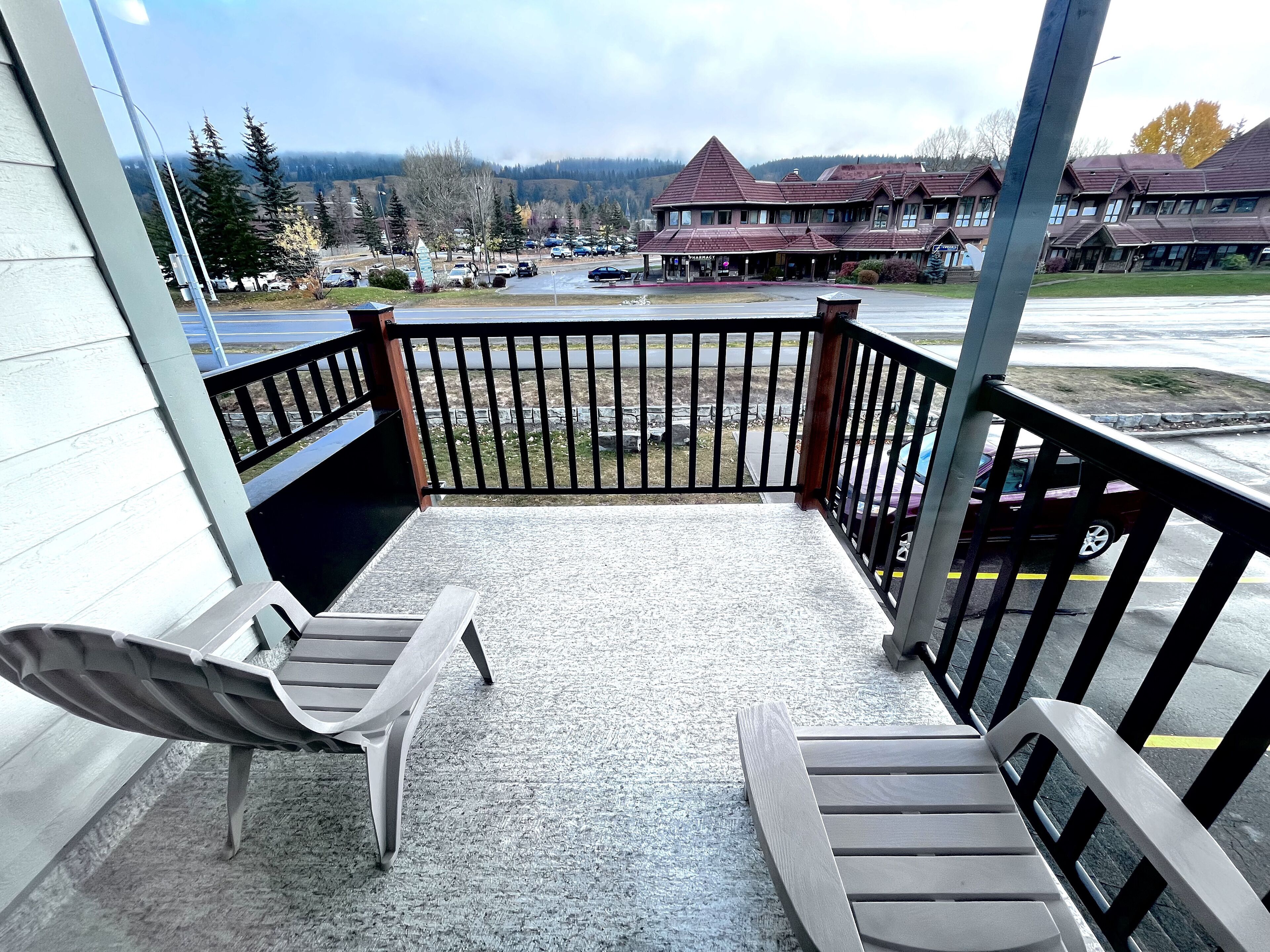 A balcony with two chairs and a view of a parking lot and buildings.