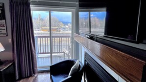 A room with a large window, a flat-screen TV mounted on the wall, a black leather chair, and a wooden cabinet. - Canadian Rockies Chalets by Trilink (Canmore)