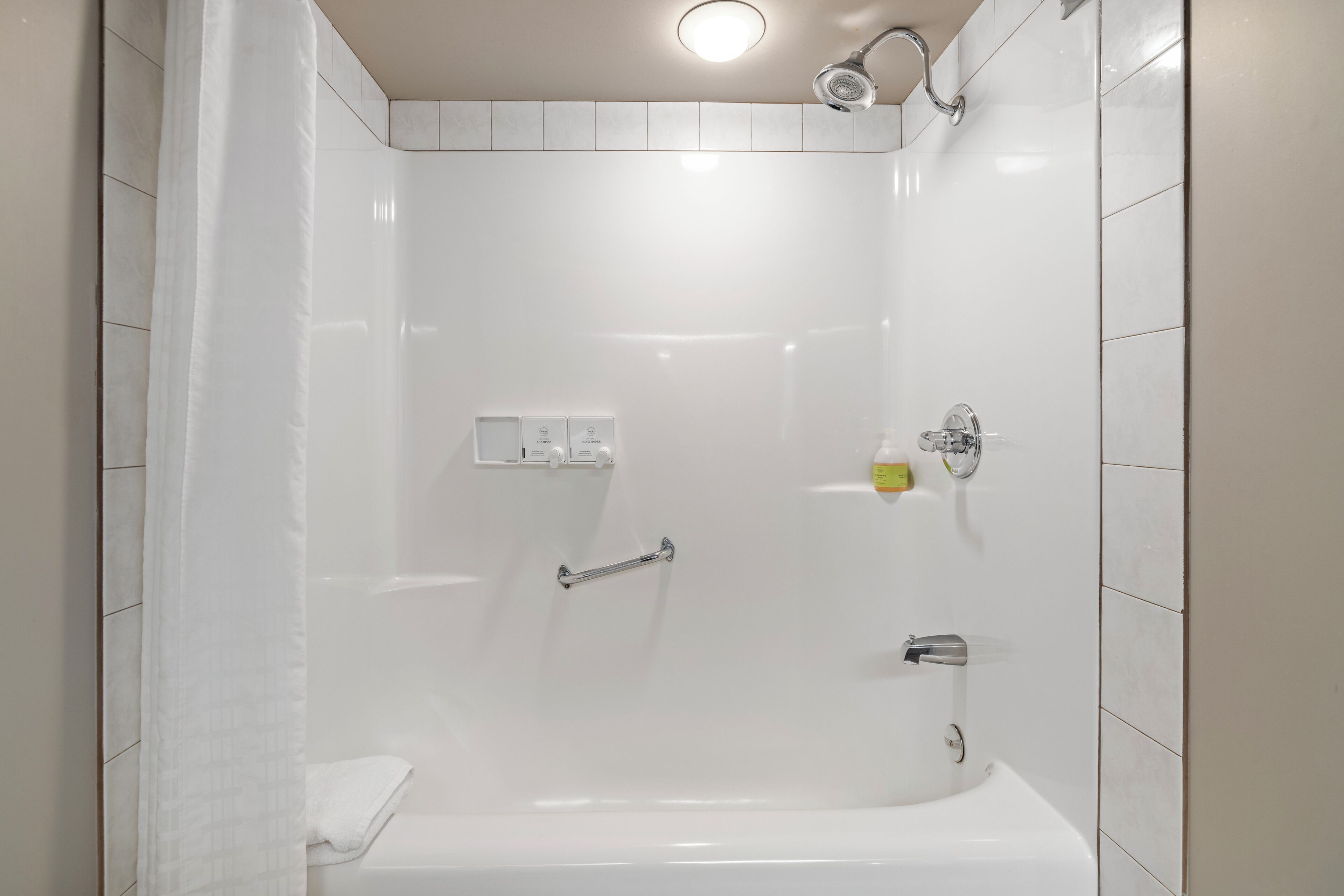 A modern bathroom with a bathtub, a shower head, and a handrail.