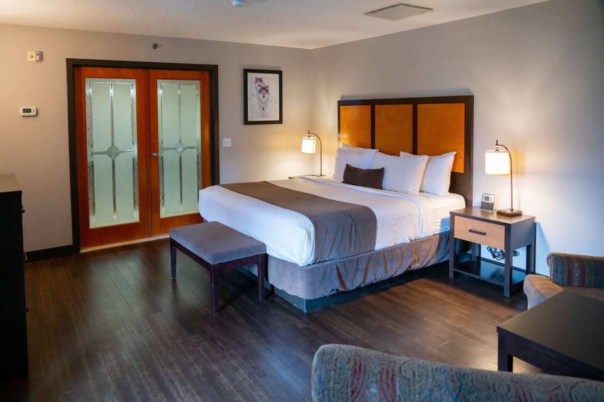 A hotel room with a large bed, bedside tables with lamps, a bench, and a door with frosted glass panels.