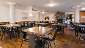 Un grand espace dédié à la salle à manger, avec plusieurs tables et chaises, une cheminée en pierre et un téléviseur fixé au mur.