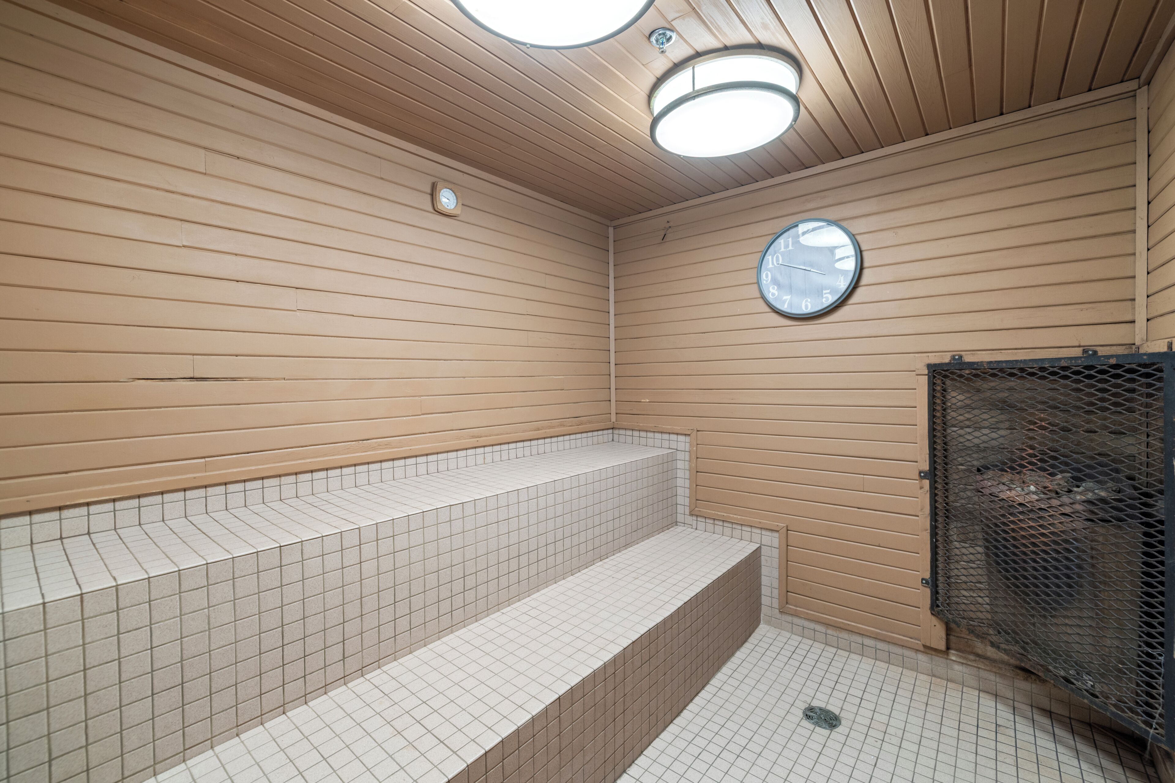 Une salle de bain avec des murs lambrissés en bois, un sol carrelé, un lavabo avec un miroir et un espace douche.