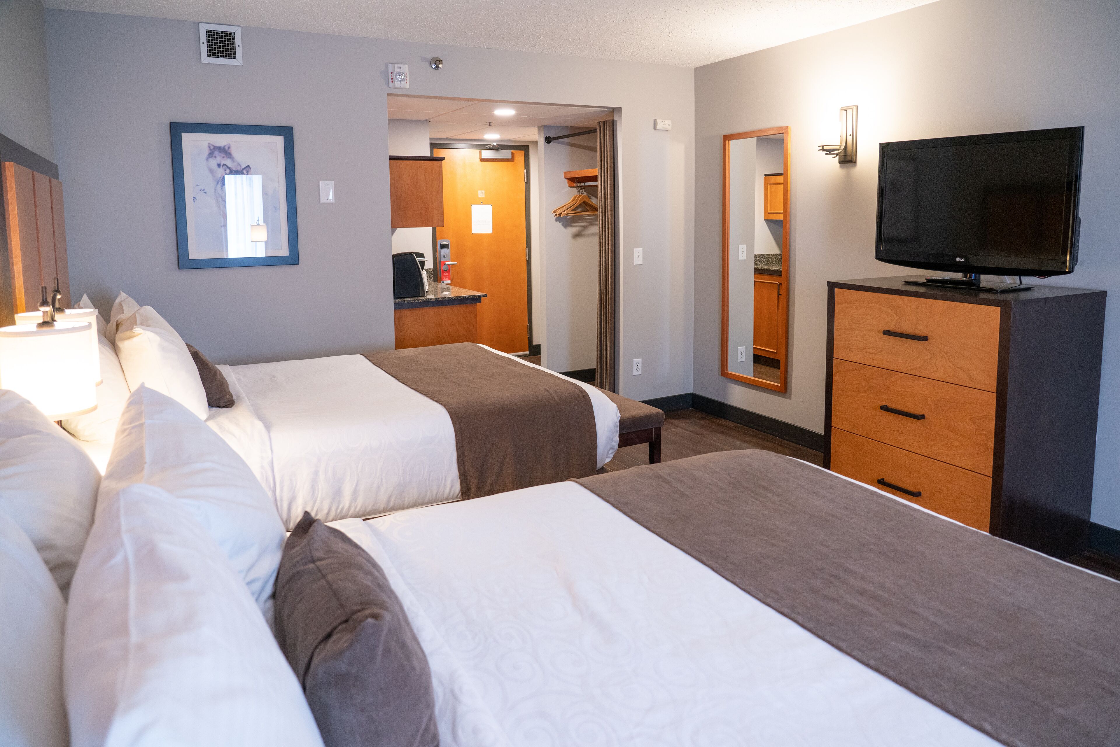A hotel room with two beds, a TV, a mirror, and a bathroom visible through an open door.