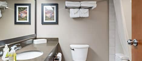 Ein Badezimmer mit Waschbecken, Toilette und Dusche. An der Wand hängen Bilder in Rahmen, und ein Handtuchhalter mit Handtüchern ist vorhanden.