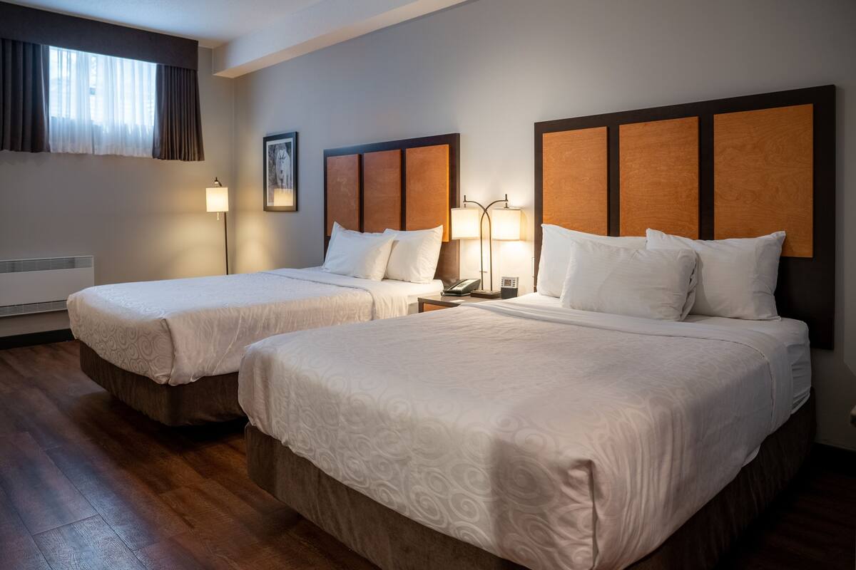 A hotel room with two beds, wooden headboards, and a large window with curtains.