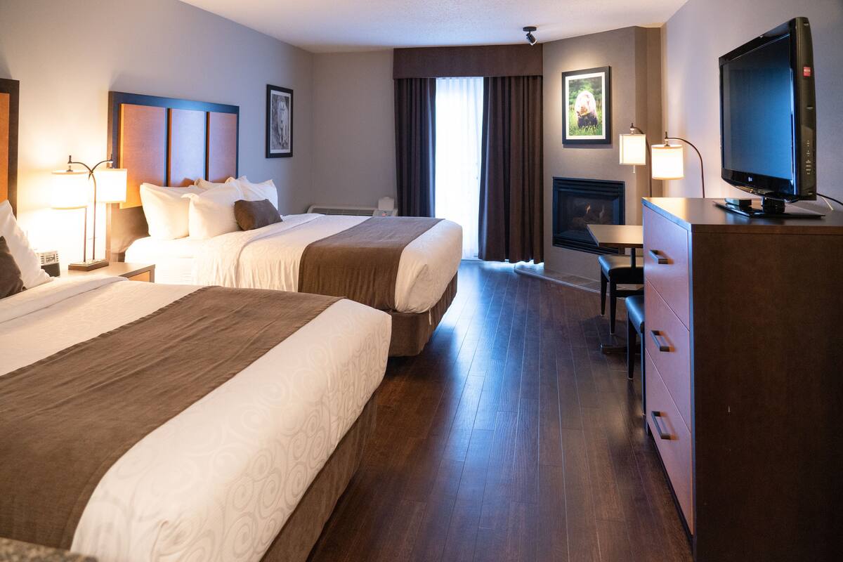 A hotel room with two beds, a desk, a television, and a fireplace.