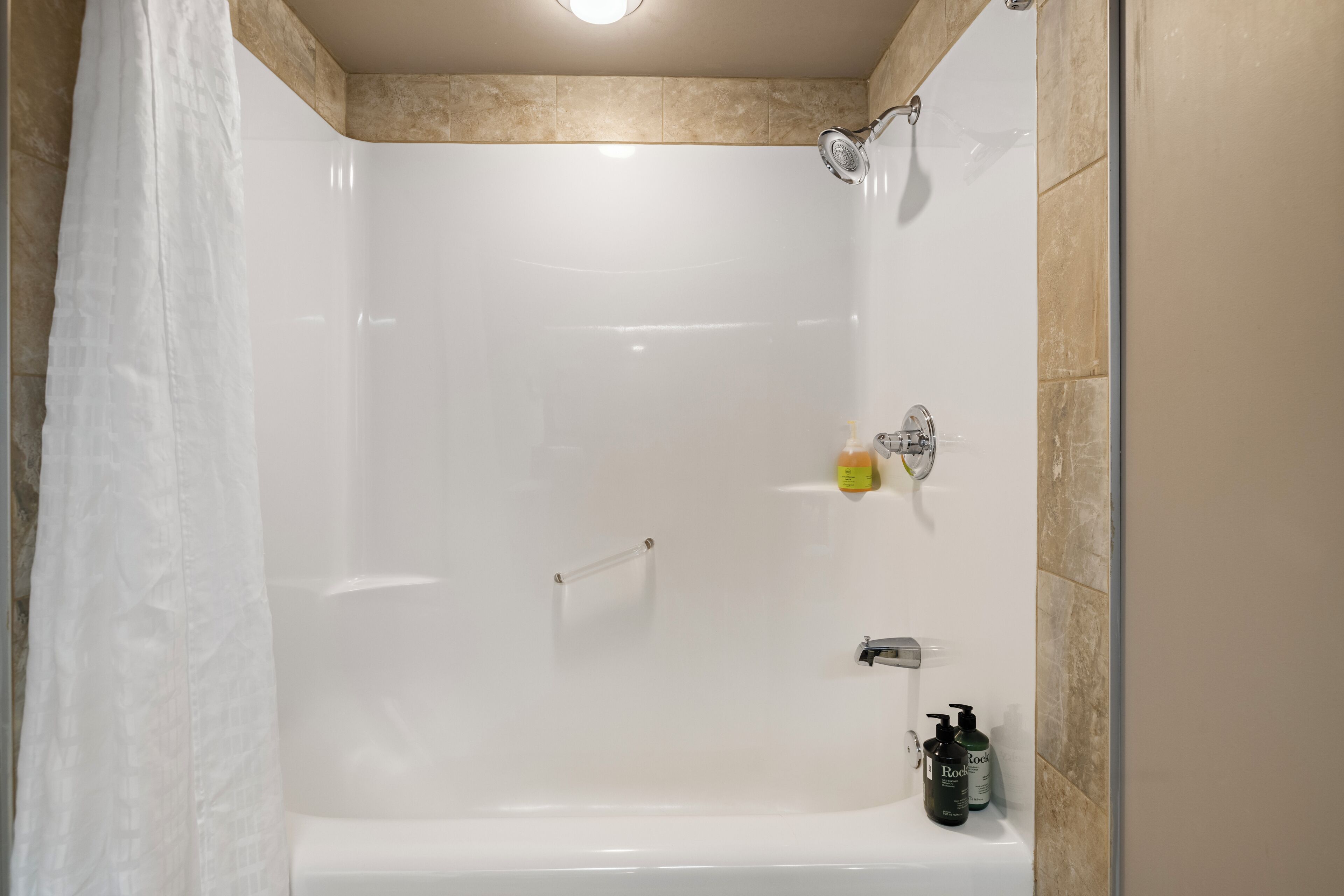 Una doccia moderna con porta in vetro, soffione a mano e una bottiglia di shampoo a parete.