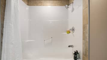 Una doccia moderna con porta in vetro, soffione a mano e una bottiglia di shampoo a parete.
