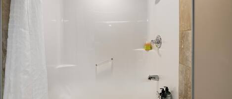 Una ducha moderna con puerta de vidrio, un cabezal de ducha de mano y una botella de champú en la pared.
