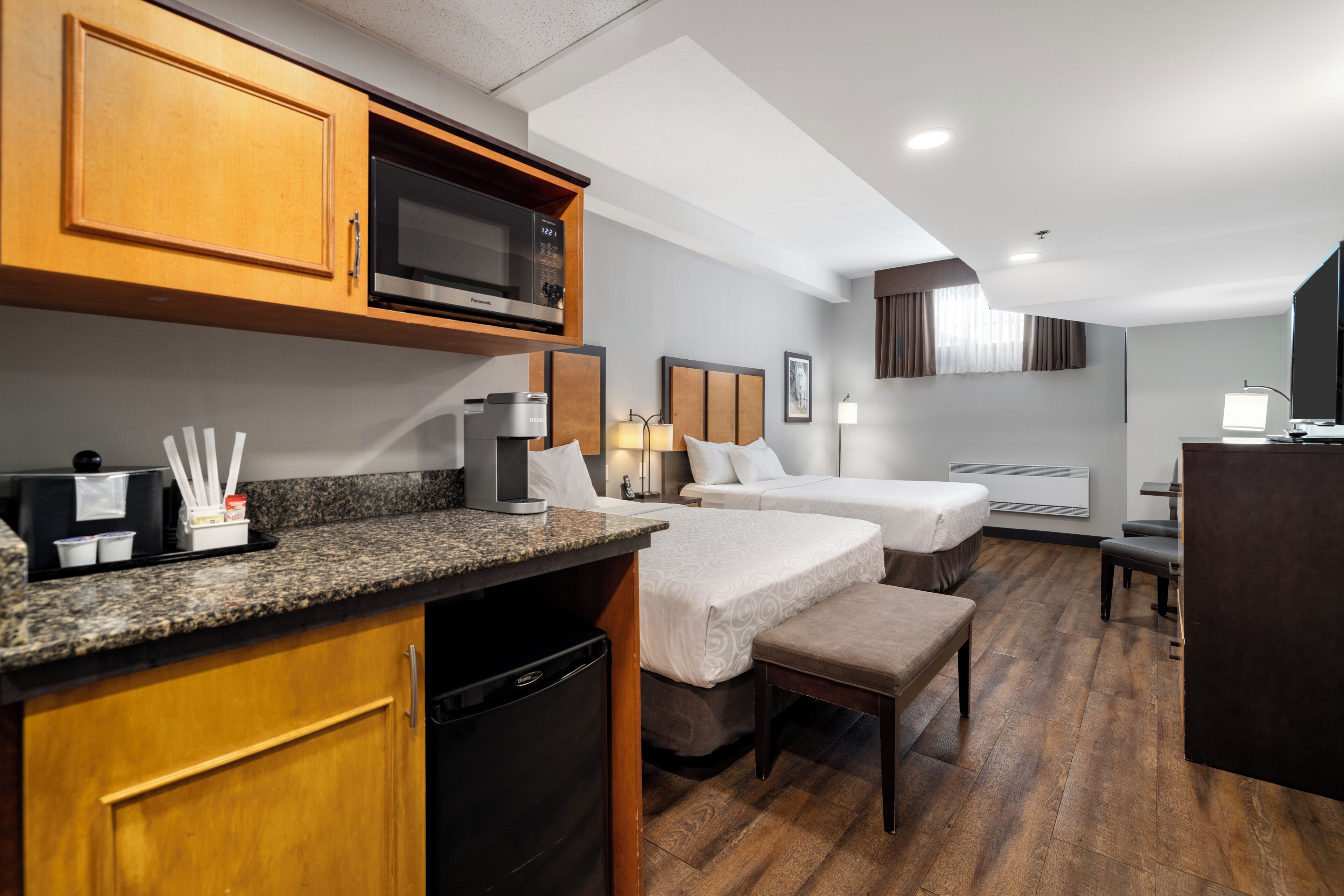 Habitación de hotel con kitchenette, dos camas, escritorio y baño.