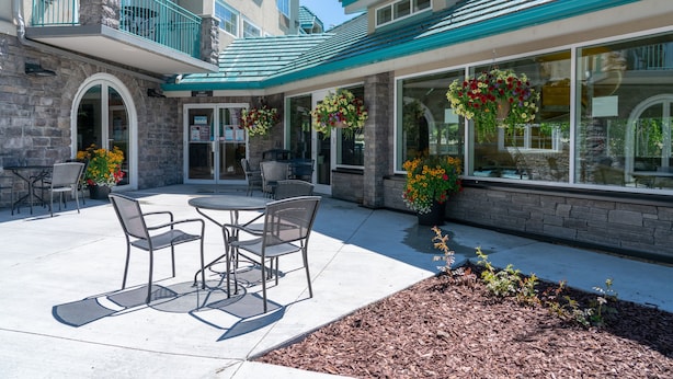 A hotel exterior with a patio area featuring outdoor seating, stone walls, and hanging flower baskets. - Pocaterra Inn and Waterslide (Canmore)