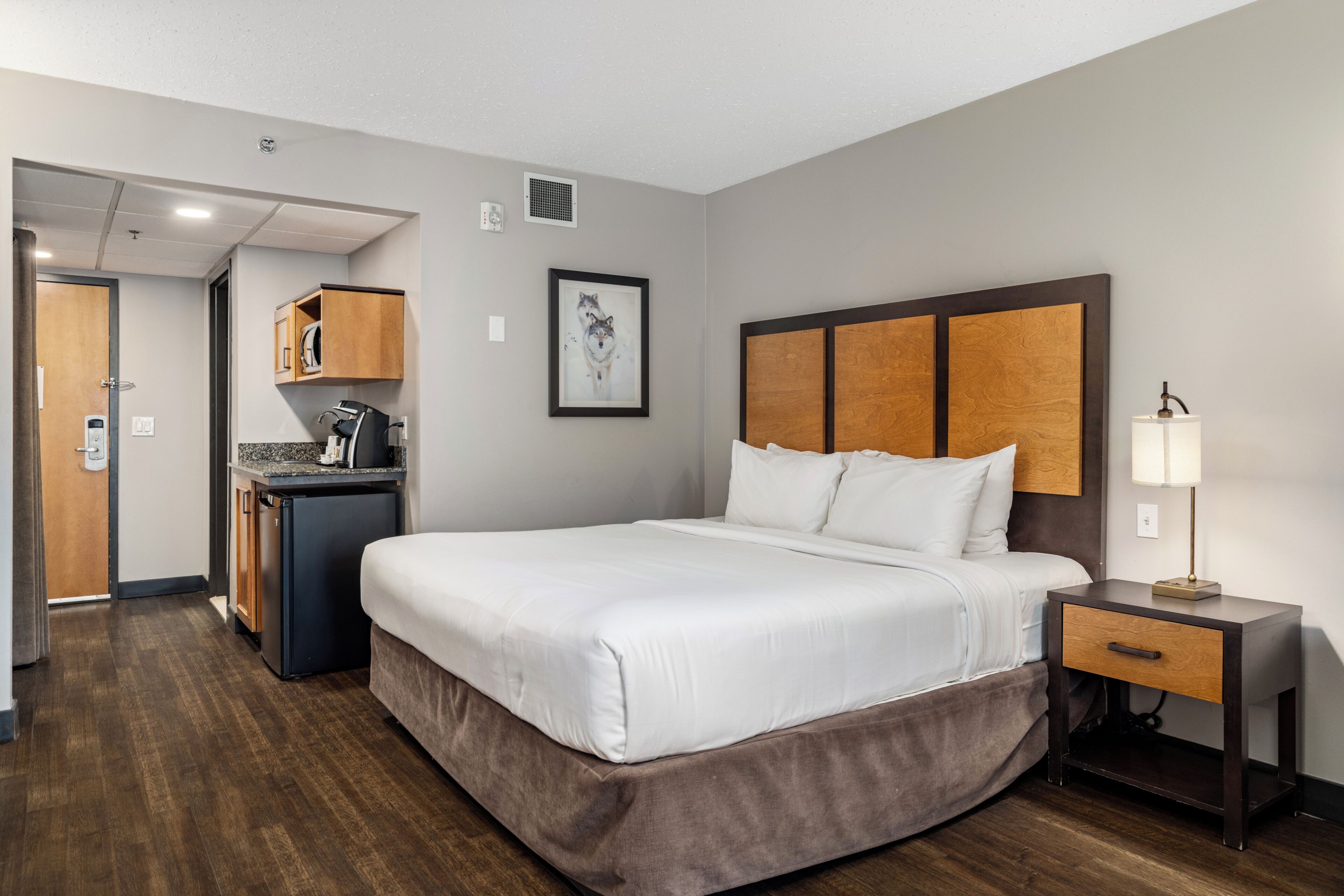 Una habitación de hotel con cama, mesita de noche y un pequeño escritorio con lámpara.