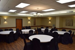 Une salle de conférence dotée de plusieurs tables rondes et de chaises, et équipée de luminaires au plafond et d’appliques murales.