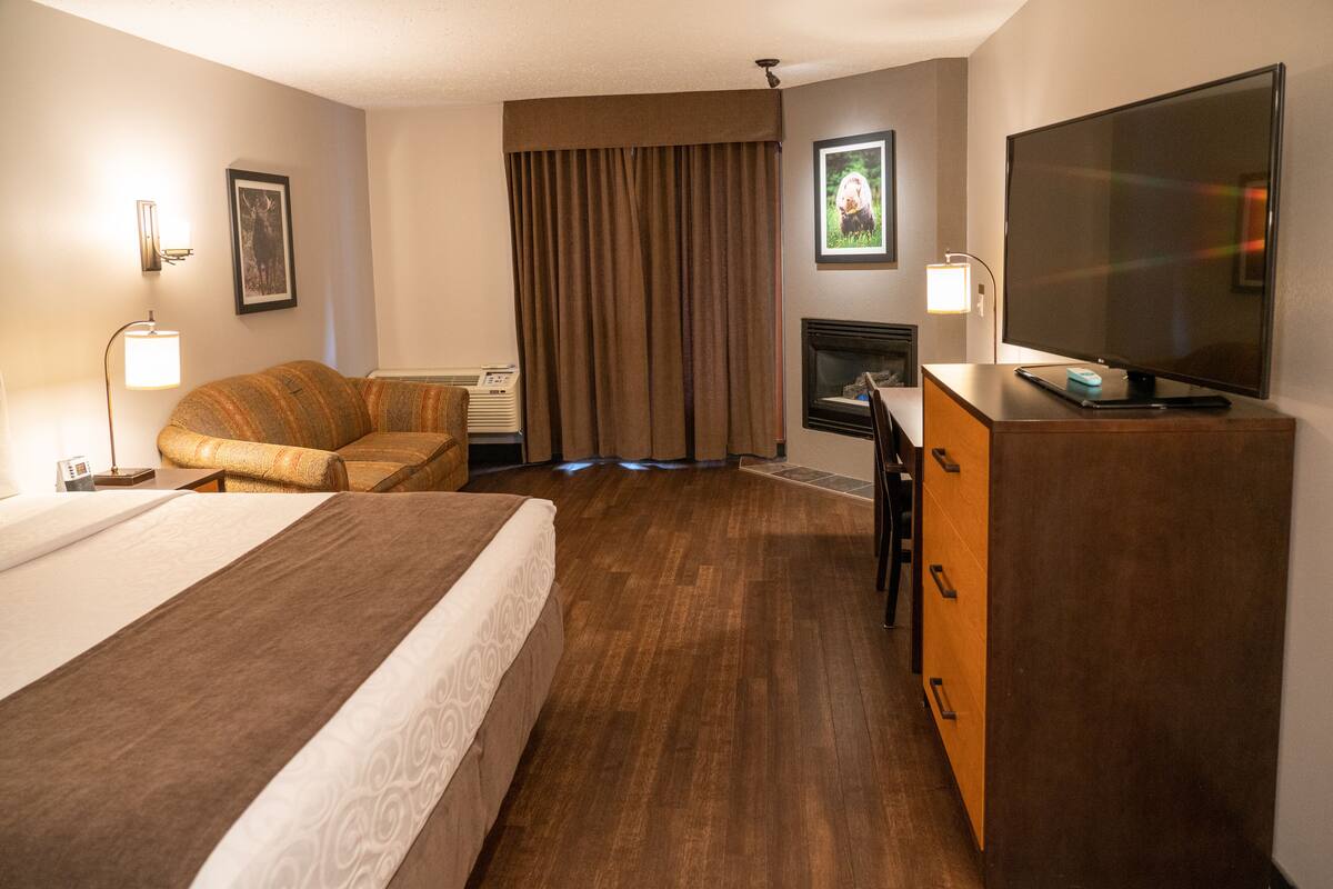 A hotel room with a large bed, a desk, a flat-screen TV, a fireplace, and a sofa.