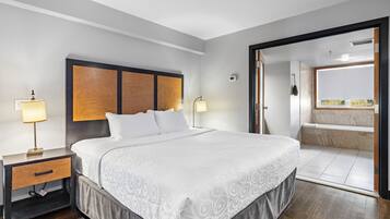Habitación de hotel con una cama grande, mesitas de noche, una lámpara y vistas al baño.