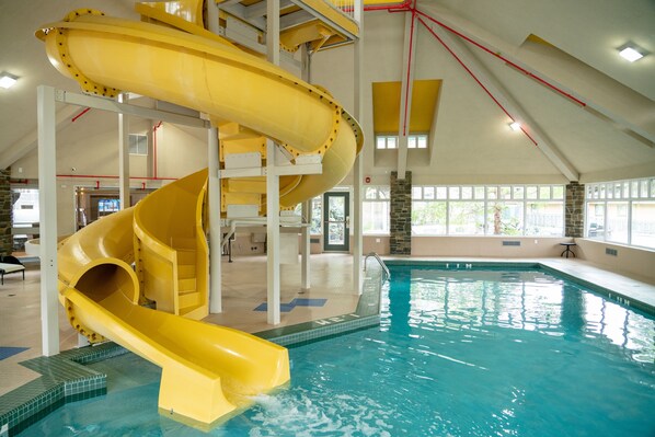 Una gran piscina interior con un tobogán amarillo y un techo alto.