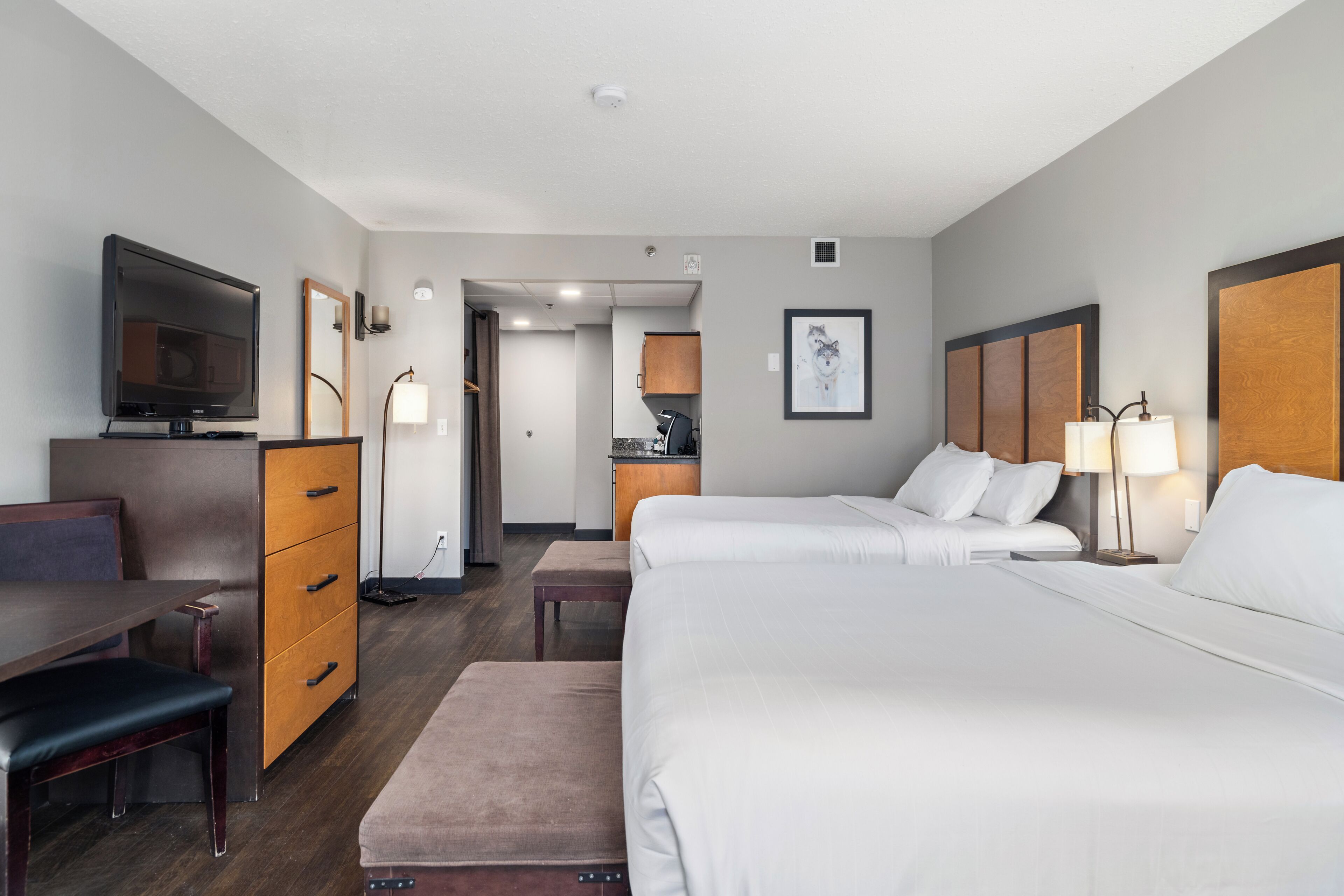 Ein Hotelzimmer mit zwei Betten, einem Schreibtisch, einem Fernseher, einem Schminktisch und einem durchgegangenen Tür erkennbaren Badezimmer.