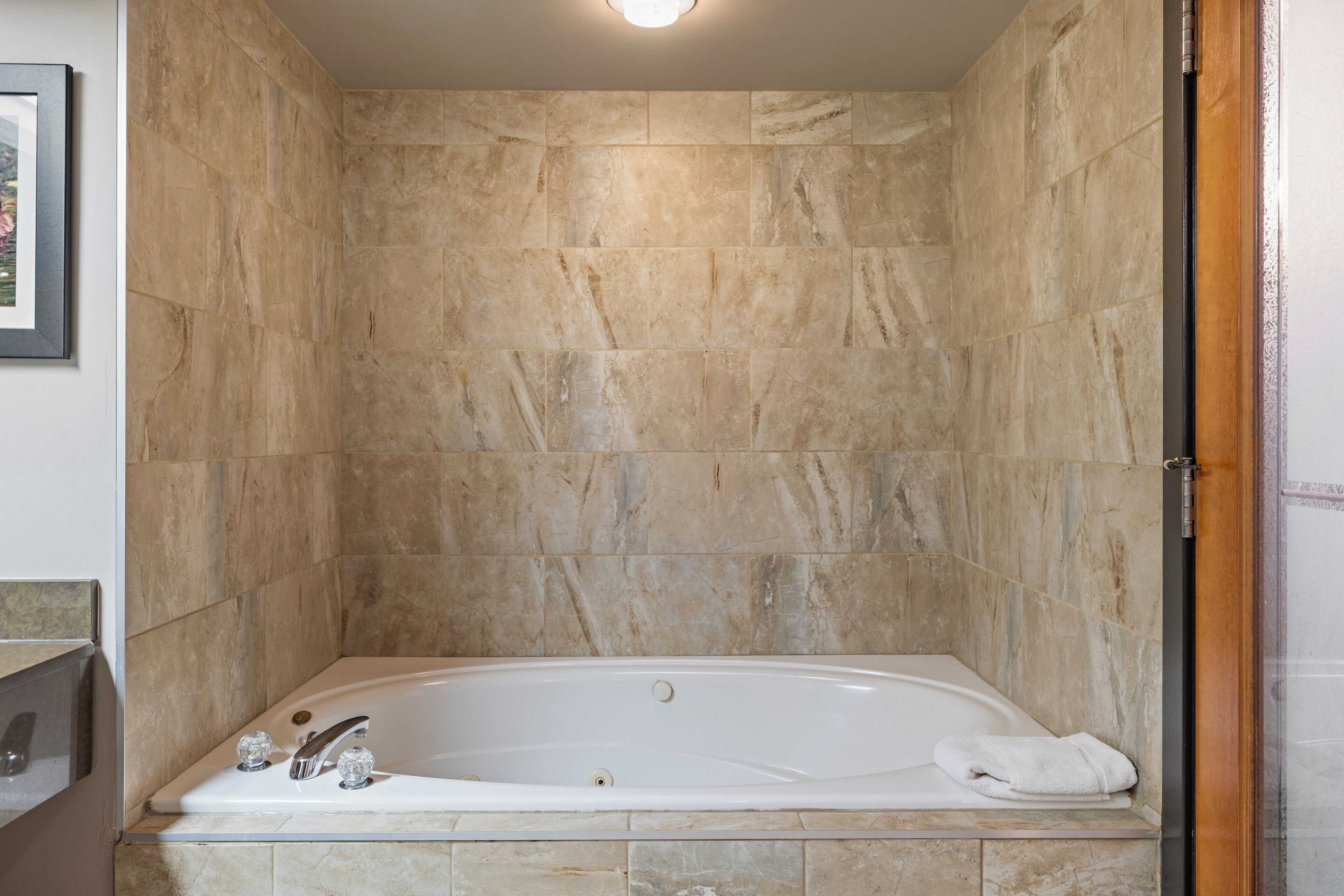 Un baño con una bañera independiente, paredes de mármol y un cuadro en la pared.